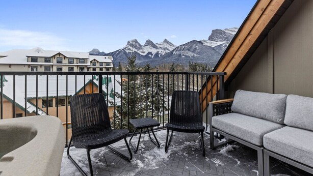 A balcony with two black chairs and a grey sofa, overlooking snow-capped mountains. - NEW Private Hot Tub ~ Upscale Mountain Home (Canmore)