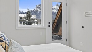 Ein Schlafzimmer mit großem Fenster und Bergblick, einer Tür mit Holzrahmen und einem weißen Bett.