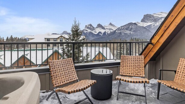 Ein Balkon mit Korbstühlen und einem runden Tisch mit Blick auf schneebedeckte Berge.