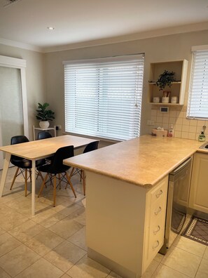 A kitchen with a central island, a dining table with chairs, a potted plant, and a built-in dishwasher. - Private and Secure, 3 bed 1.5 bath (Kardinya)