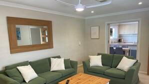 A living room with two green sofas, a wooden coffee table, a large mirror, and a kitchen visible through an open door. - Private and Secure, 3 bed 1.5 bath  (Kardinya)