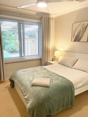 A bedroom with a bed, a nightstand, a lamp, a window with curtains, and a painting on the wall. - Private and Secure, 3 bed 1.5 bath (Kardinya)