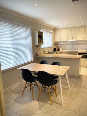 A modern kitchen with a dining area, featuring a wooden table, black chairs, and a built-in island with a sink. - Private and Secure, 3 bed 1.5 bath (Kardinya)
