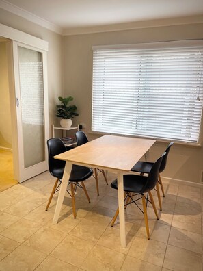 A dining area with a table and chairs, a potted plant, and a window with blinds. - Private and Secure, 3 bed 1.5 bath  (Kardinya)