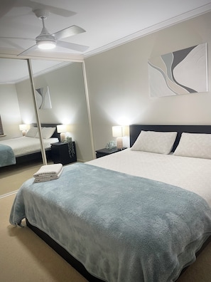 A hotel room with a large bed, a ceiling fan, a nightstand with a lamp, and a mirror on the wall. - Private and Secure, 3 bed 1.5 bath (Kardinya)