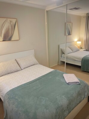 A hotel room with a large bed, a bedside table with a lamp, and a mirror on the wall. - Private and Secure, 3 bed 1.5 bath  (Kardinya)