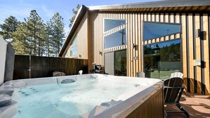 A wooden deck with a hot tub, outdoor seating, and a glass door leading to a covered area. - Brand New Gorgeous home in fantastic Big Bear Lake right on Snow summit Resort! (Big Bear Lake)