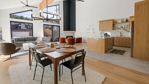 A modern kitchen with wooden cabinets, a dining area with a large table and chairs, and a view of the outside through large windows. - Brand New Gorgeous home in fantastic Big Bear Lake right on Snow summit Resort! (Big Bear Lake)