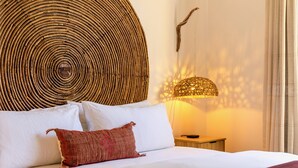 A neatly made bed with white and red pillows, a woven wall art piece, and a lamp casting a warm glow. - 3 Bd Penthouse in the heart of San Jose Del Cabo (San Jose del Cabo)