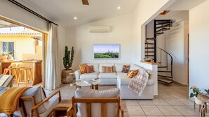 A spacious living room with a sofa set, a coffee table, and a TV mounted on the wall. There is a staircase with a metal railing leading to an upper floor. - 3 Bd Penthouse in the heart of San Jose Del Cabo (San Jose del Cabo)