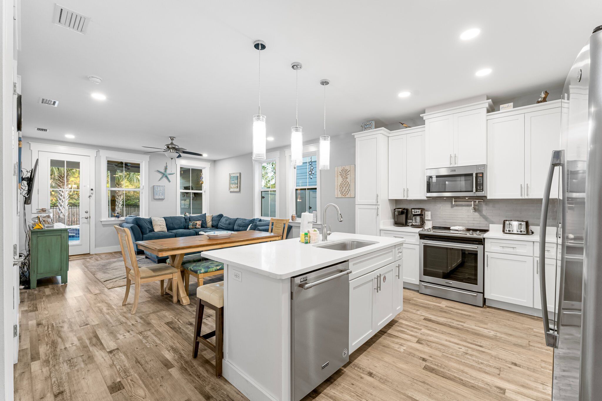 A modern kitchen with white cabinets, stainless steel appliances, and a wooden dining area.
