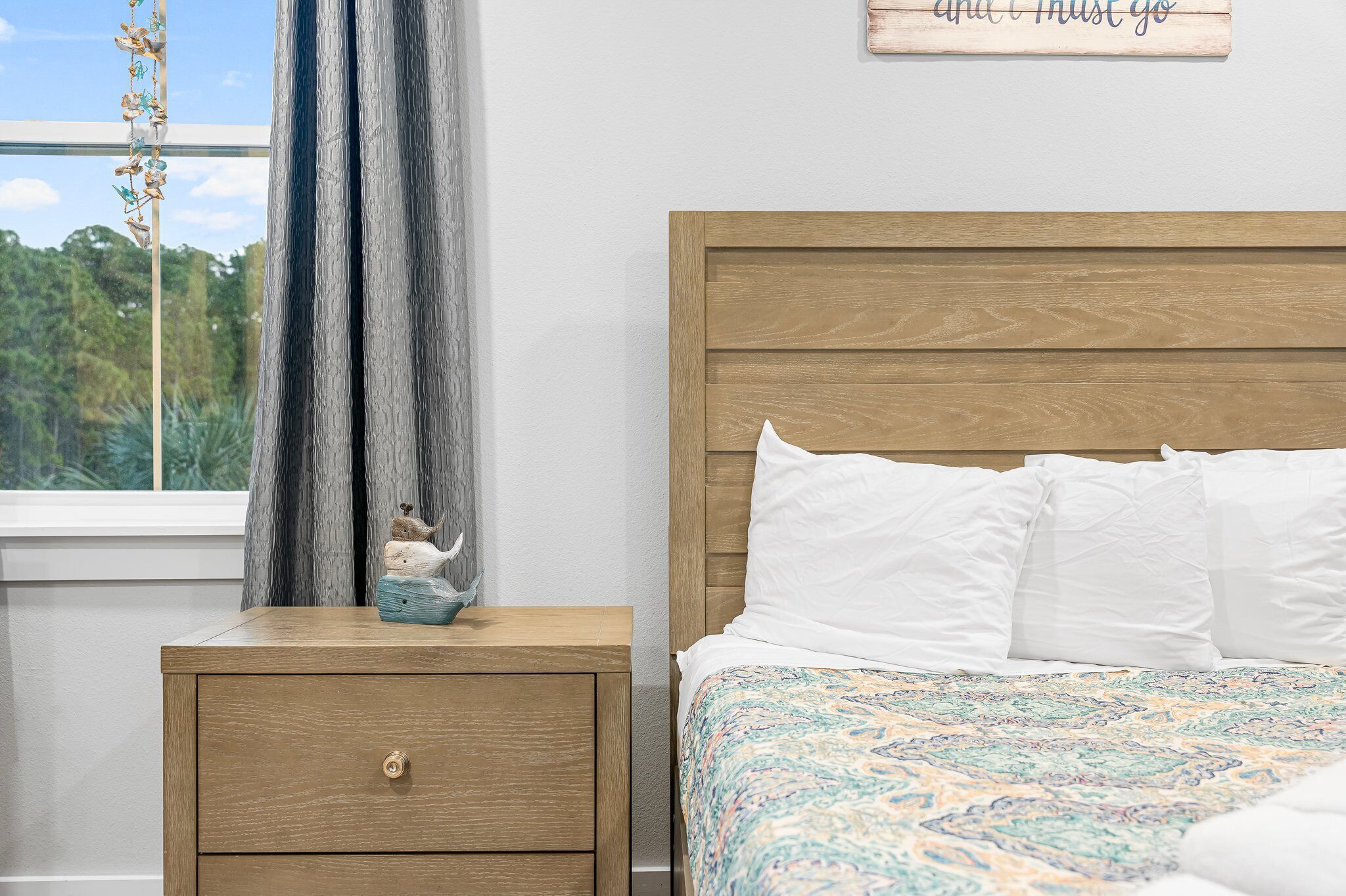 Ein Schlafzimmer mit Holzkopfende, einem Bett mit weißen Kissen, einem Nachttisch mit Schublade und einem Fenster mit Vorhängen.