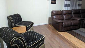 Una sala de estar con un sofá de cuero marrón, dos sillones negros con lunares y una mesa de centro de madera.