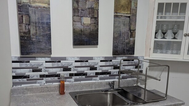 Una cocina con armarios blancos, salpicadero de mármol y tres cuadros abstractos en la pared.