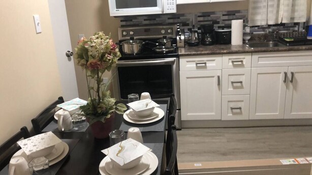 A dining area with a table set for two, a microwave, a stove, and white cabinets.