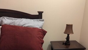 A neatly made bed with a patterned bedspread and pillows, a small wooden nightstand with a lamp, and a plain wall.