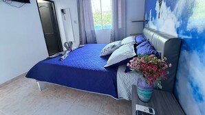 Um quarto com cama, TV fixada na parede, janela com cortinas e um vaso com flores na mesa de cabeceira.