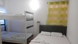 Quarto de dormitório com beliches, uma cama individual e uma janela com cortinas.