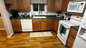 A kitchen with wooden cabinets, a white dishwasher, a stove, and a microwave. - Charming 4-bedroom home with WiFi and massage chair in fabulous Colorado Springs (Colorado Springs)