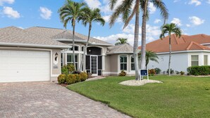 A residential house with a garage, a well-maintained lawn, and palm trees.