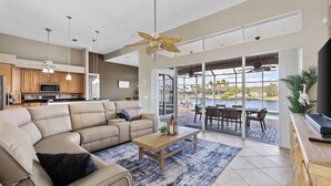 A modern living room with a beige sectional sofa, a wooden coffee table, and a view of a pool through large sliding glass doors.