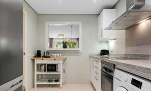 Cocina compacta con horno integrado, microondas y ventana con vistas a zonas verdes.