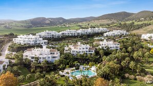 Un resort con varias construcciones blancas, una piscina central y follaje circundante.