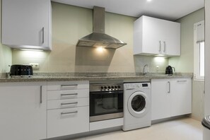 A modern kitchen with white cabinets, a stainless steel range hood, a built-in oven, a washing machine, and a coffee maker. - Casa Sereno | lagoon - pool - garden - view (Casares)