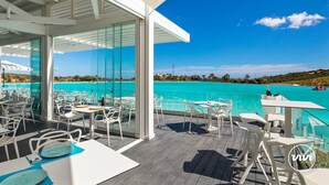 Un espacio al aire libre con mesas y sillas, con vista al mar turquesa y un cielo despejado.