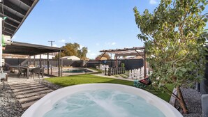Un jacuzzi en un patio trasero con una terraza, un tablero de ajedrez y una pérgola.