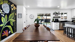 Una cocina moderna con armarios blancos, una mesa de comedor de madera y un mural floral blanco y negro en la pared.