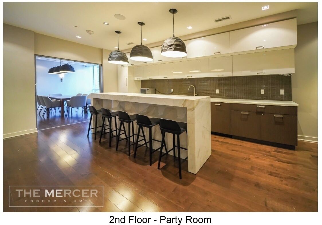 A modern kitchen with bar stools, pendant lighting, and a view to a dining area.