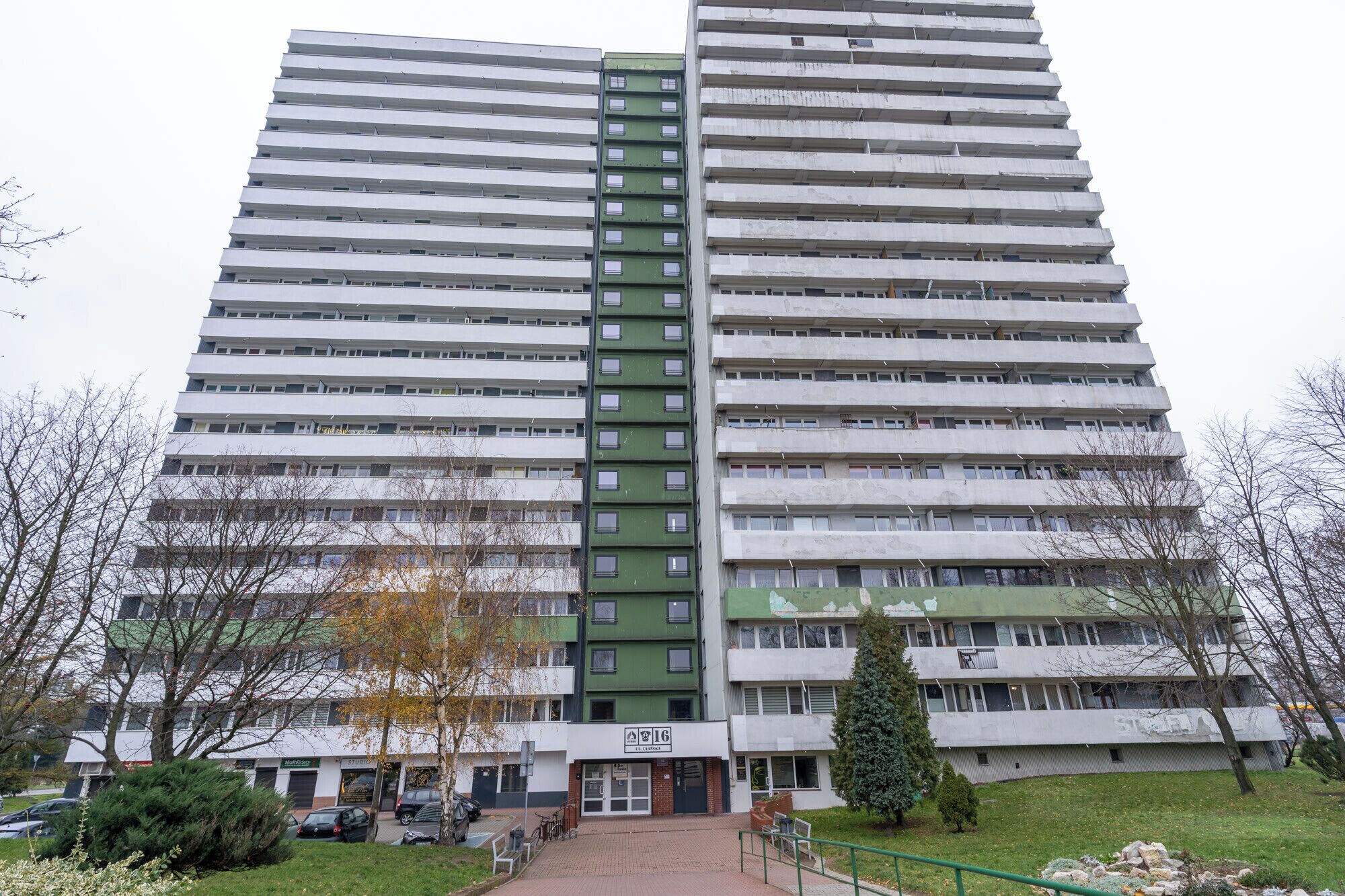 Korkea kerrostalo, jossa on useita kerroksia, ja jossa on keskeinen viheralue sekä valkoisista ja vihreistä sävyistä koostuva julkisivu.