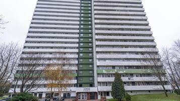 Korkea kerrostalo, jossa on useita kerroksia, ja jossa on keskeinen viheralue sekä valkoisista ja vihreistä sävyistä koostuva julkisivu.