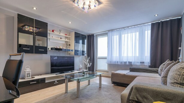A modern living room with a glass coffee table, a sofa, a TV, and built-in shelves. - Park Śląski 18th Floor Apartment (Katowice)