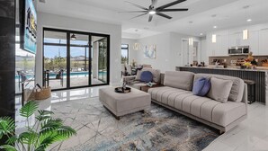 Una sala de estar moderna con un sofá, un reposapiés y un gran ventanal con vista a una piscina.