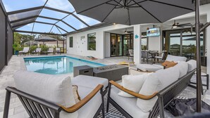 Un área de piscina moderna al aire libre con un patio de cristal, sillas de descanso y zona de comedor.