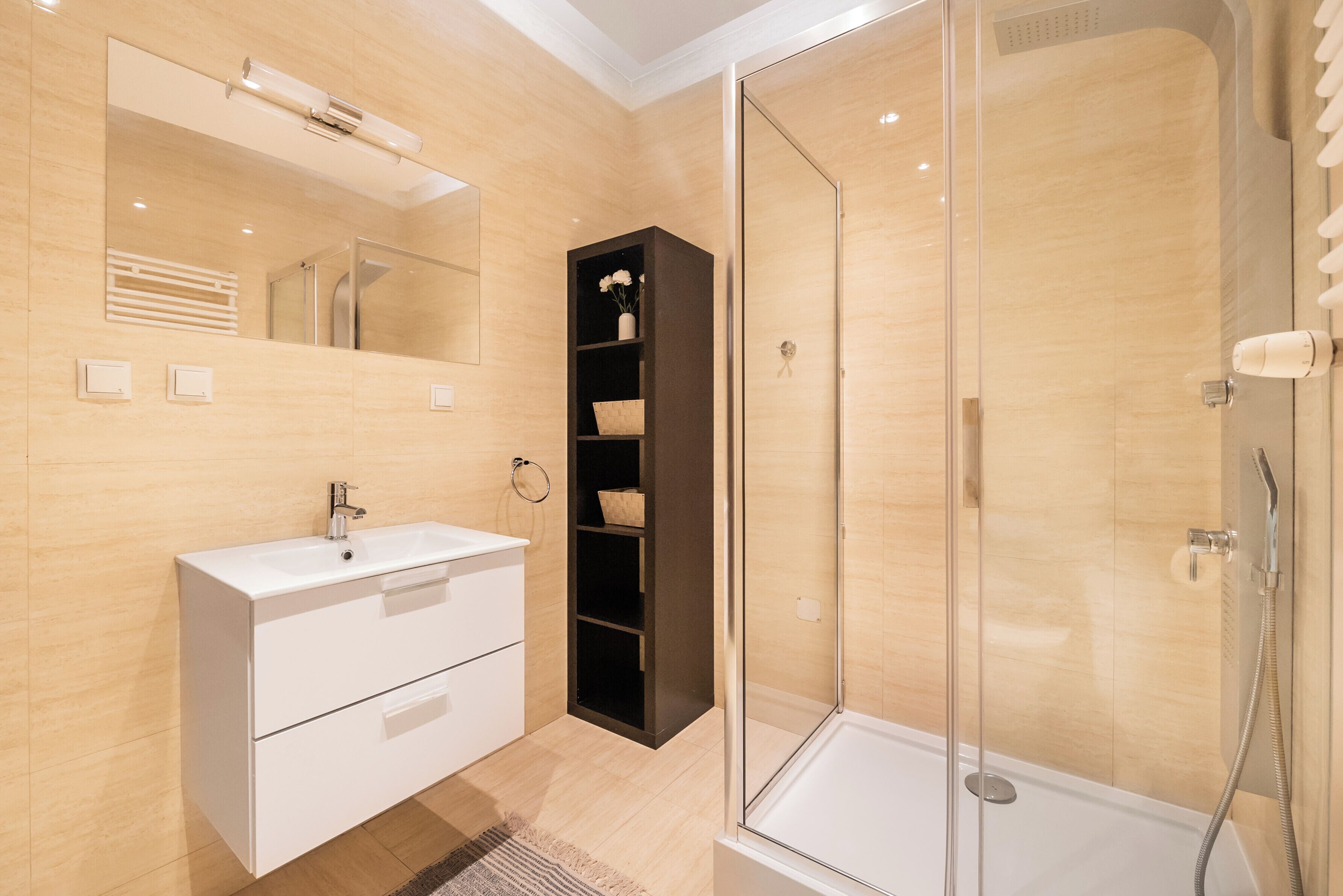 Ein modernes Badezimmer mit einem weißen Waschtisch, einer Duschkabine aus Glas und einem Holzregal.