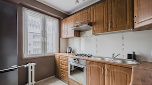 A kitchen with wooden cabinets, a gas stove, a sink, and a window with lace curtains.