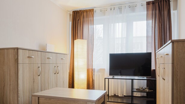 A hotel room with a bed, a desk, a television, and wooden cabinets.
