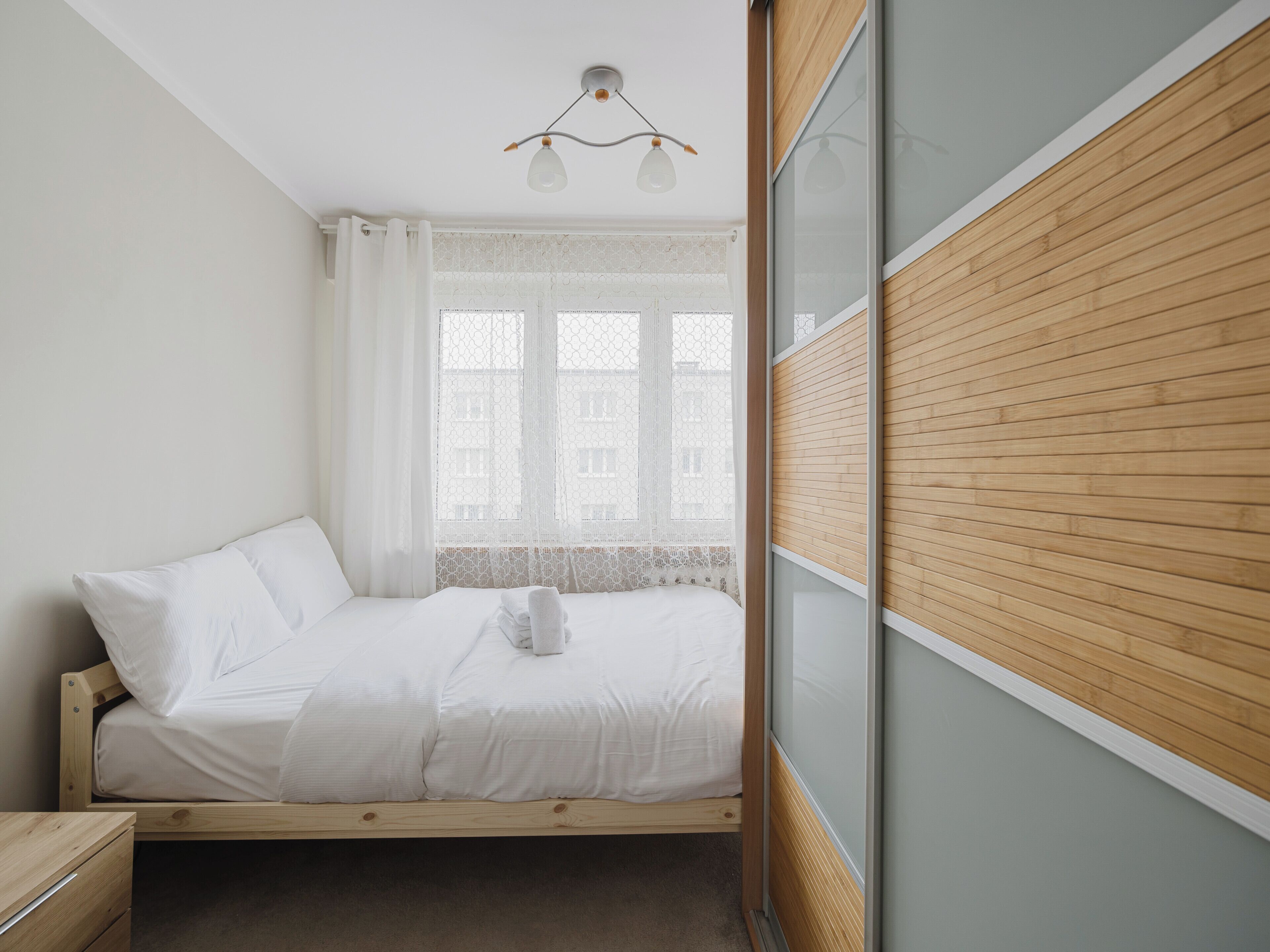 Un lit bien fait, avec du linge de lit blanc, une tête de lit en bois et une table de chevet dotée d’un tiroir.