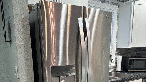 Ein Edelstahl-Kühlschrank in einer Küche mit weißen Schränken, einer Mikrowelle und einem gemusterten Teppich.