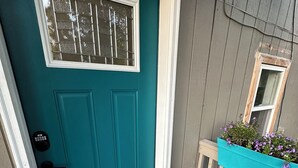 Eine türkisblaue Tür mit Fenster, Klingel und Fußmatte.