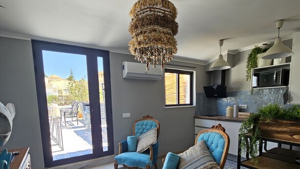 A spacious living room with a large window, two blue armchairs, a wooden coffee table, and a chandelier.