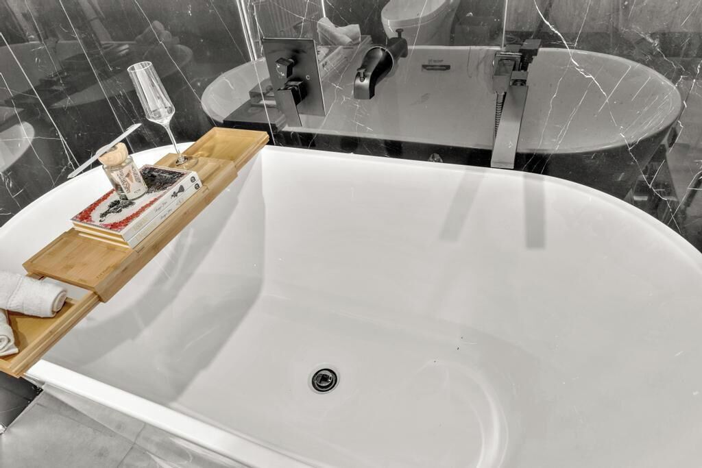 A modern bathroom with a freestanding bathtub, a glass-enclosed vanity, and a marble-tiled wall.