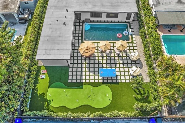Vista aerea di una piscina sul tetto con una piccola vasca, sedie a sdraio, ombrelloni e un campo da golf.
