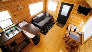 Eine gemütliche Holzblockhütte mit Küchenzeile, einer Sitzecke, einem Esstisch und einem an der Wand befestigten Fernseher.