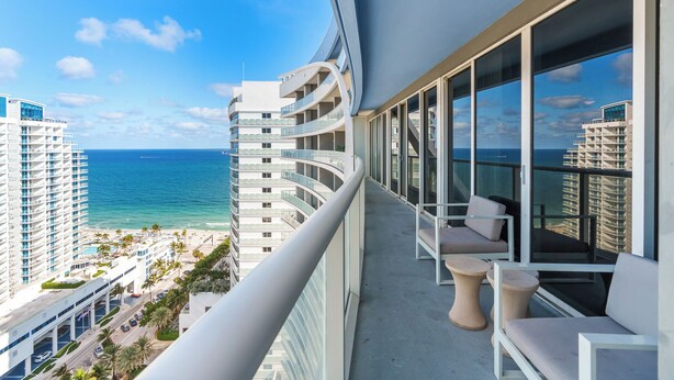 Un balcon doté d’une balustrade incurvée, donnant sur une plage et l’océan.