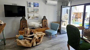Een woonkamer met een flatscreen televisie, houten meubels, een blauwe fauteuil en uitzicht op buiten.