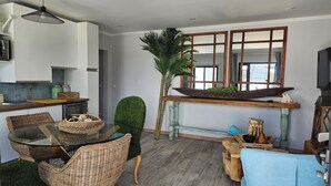Een moderne keuken met een eethoek, met een glazen tafel, rieten stoelen en een decoratieve plant.